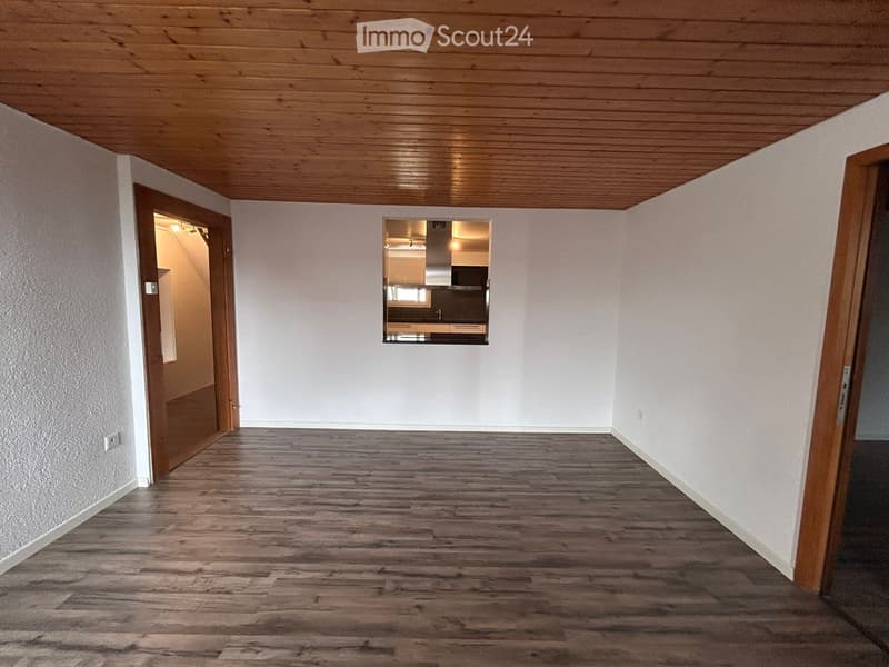 Empty room with wooden flooring and white walls, featuring a wooden ceiling and two open doors leading to other rooms.