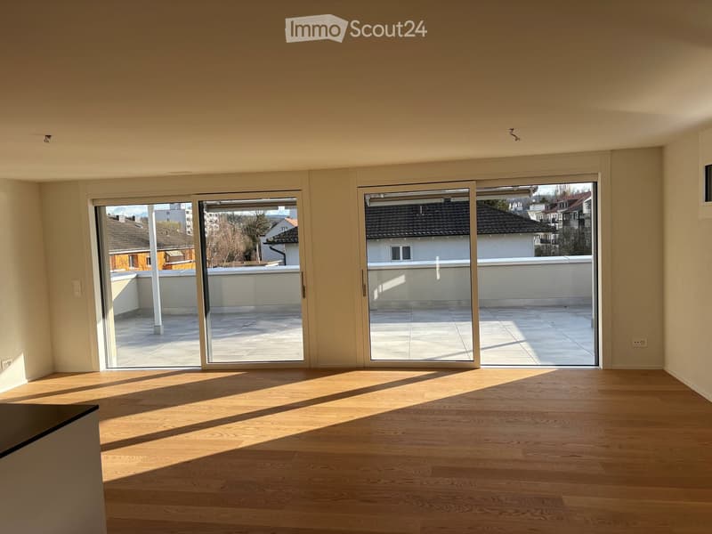 Empty room with wooden flooring, large sliding glass doors leading to a balcony, and natural light streaming in.