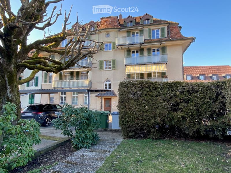 5 story building, beige walls, multiple balconies, brown shutters, green awnings, car parked in covered parking area