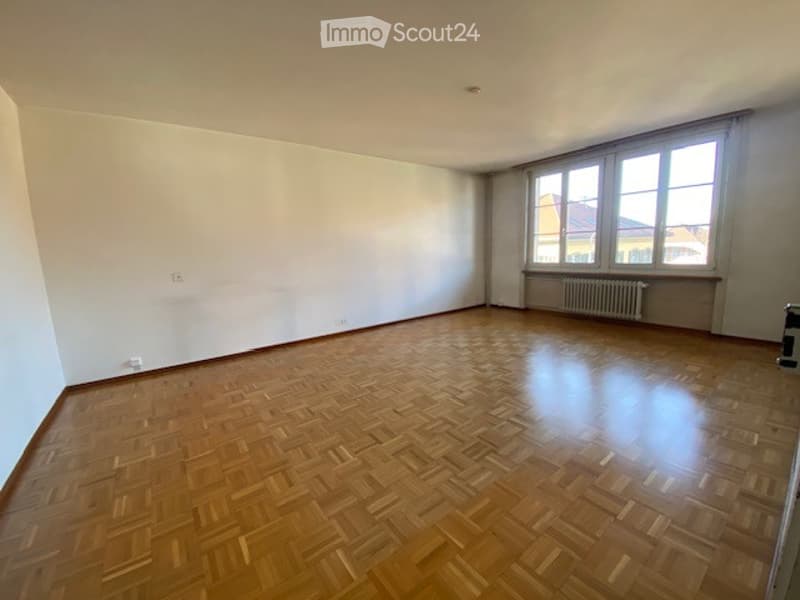 Unfurnished Room. Completely empty room with wooden parquet flooring, white walls, and large windows with curtains. No furniture or equipment present.