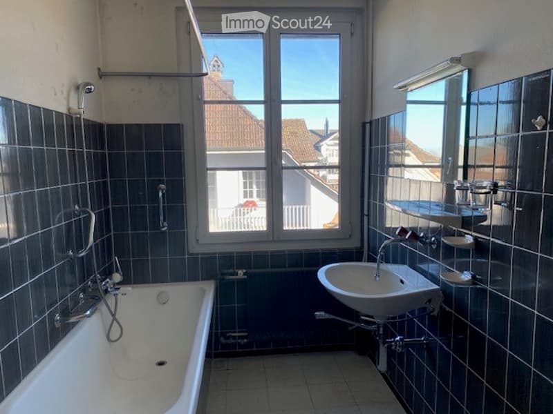 A bathroom with a bathtub, sink, shower, and window, all set against black tiled walls.