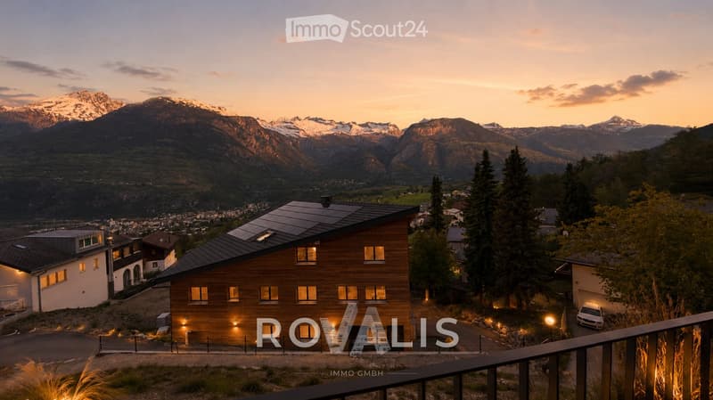 A modern wooden house with solar panels on the roof, situated in a scenic valley with snow-capped mountains in the background.