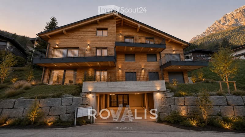 Modern two-story house with wooden facade, large windows, balconies, and a stone entrance area. Surrounded by greenery and mountains.