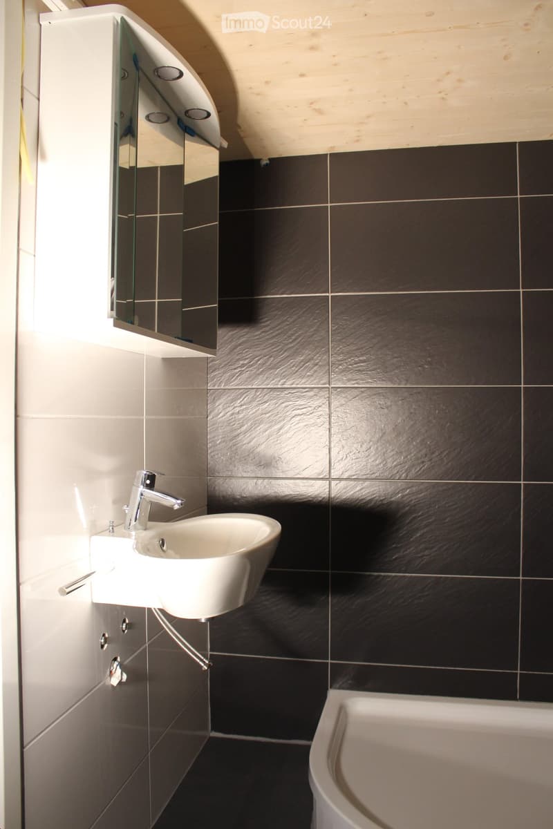 Modern bathroom with a white sink, chrome faucet, mirrored cabinet, and dark tiled walls.