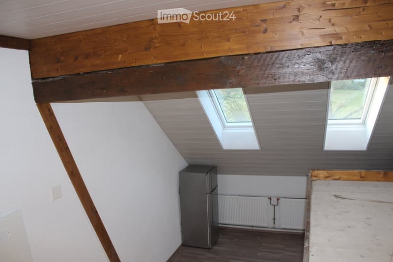 Loft-style room with wooden beams, skylights, and a refrigerator. The space features exposed wooden beams and a slanted ceiling with skylights, creating a bright and airy atmosphere.