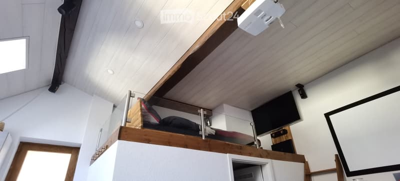 Loft-style room with a raised wooden bed platform, a large screen, a projector, and built-in cabinets.