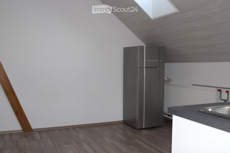 Modern kitchen with wooden flooring, white walls, stainless steel refrigerator, and a sink on the counter.