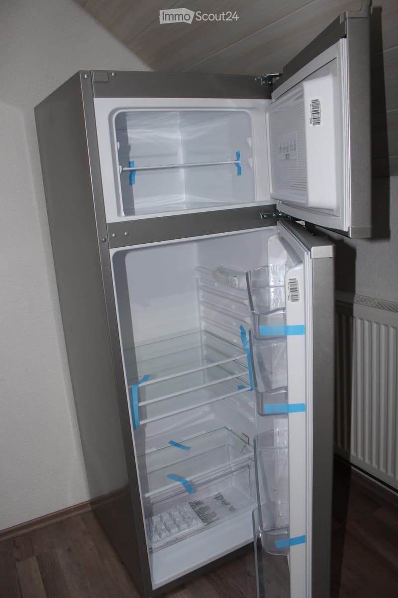A modern stainless steel refrigerator with both doors open, showing empty shelves and compartments.