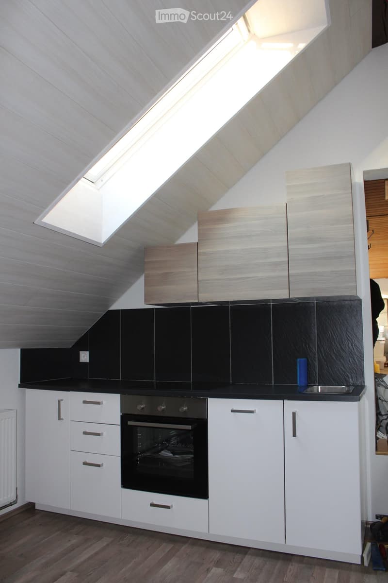 Modern kitchen with white cabinets, black countertops, and a built-in oven. Features a skylight window and sleek design.