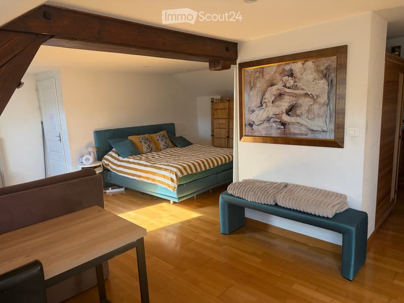 Cozy bedroom with a large bed, striped bedding, a wooden table, a bench, and a painting on the wall.