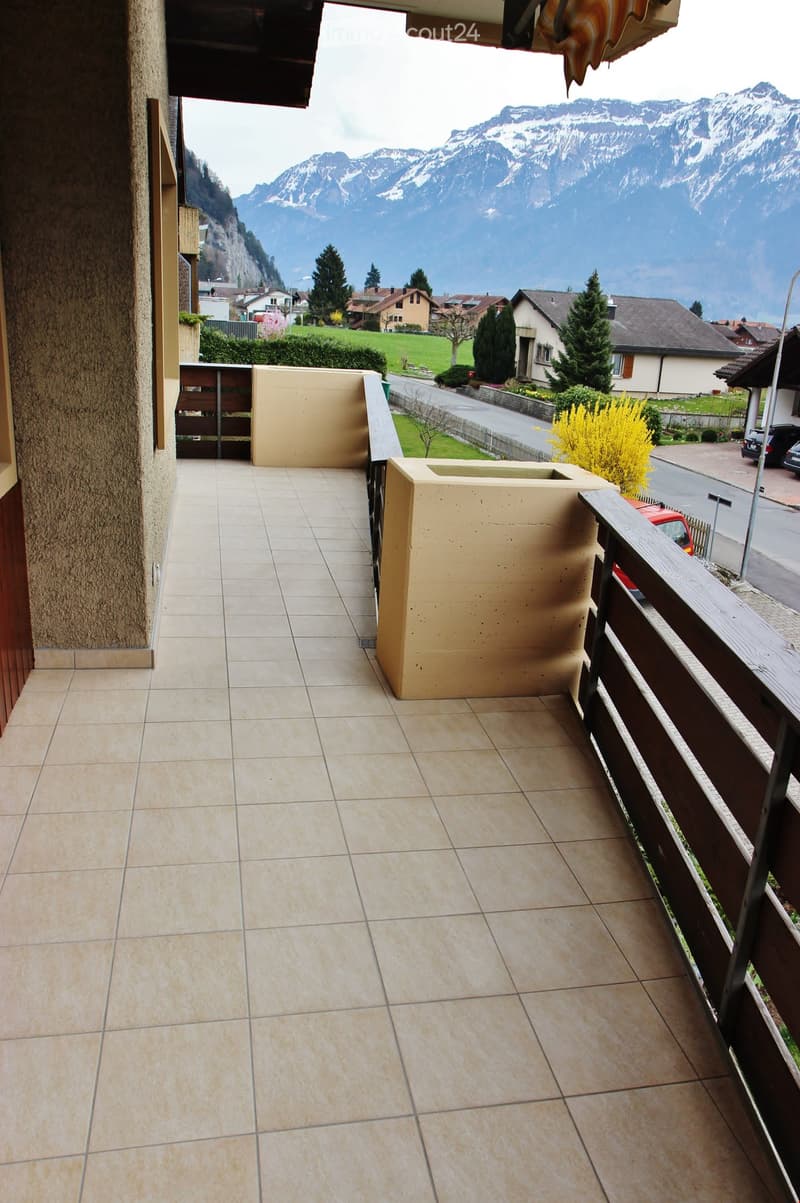 Balcony with tiled floor, wooden railing, and scenic mountain view in the background.