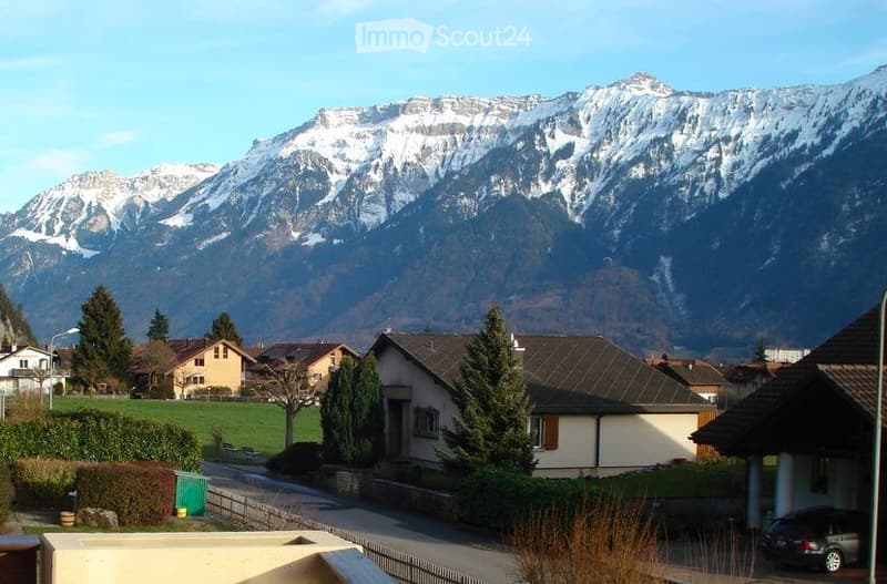 Scenic view of a residential area with houses, trees, and snow-capped mountains in the background.