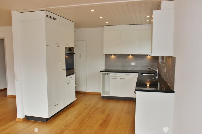 Modern kitchen with white cabinets, wooden flooring, stainless steel sink, and built-in oven.