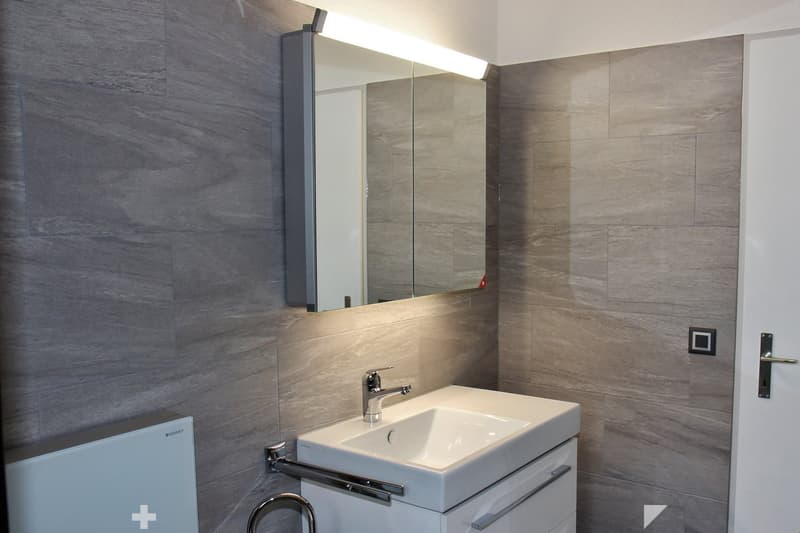 Modern bathroom with a white sink, chrome faucet, large mirror with built-in lighting, and a sleek cabinet.