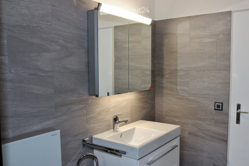 Modern bathroom with a white sink, chrome faucet, large mirror with built-in lighting, and a sleek cabinet.