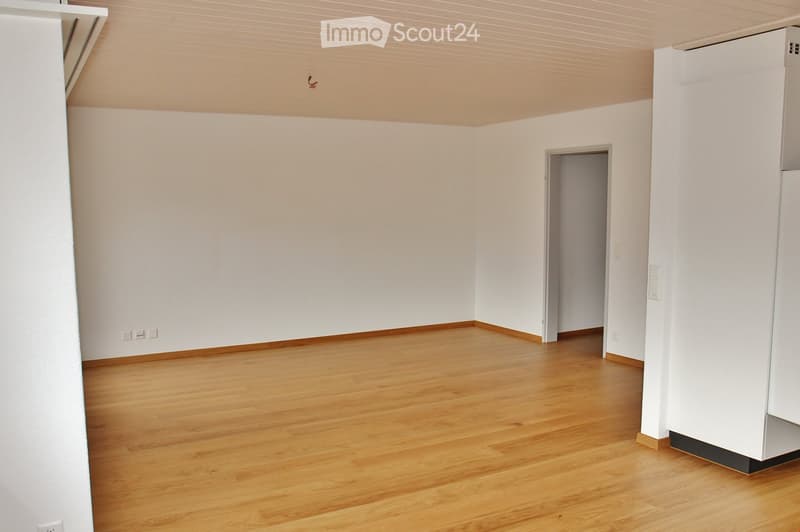 Empty room with light wooden flooring and white walls, featuring a doorway leading to another space.