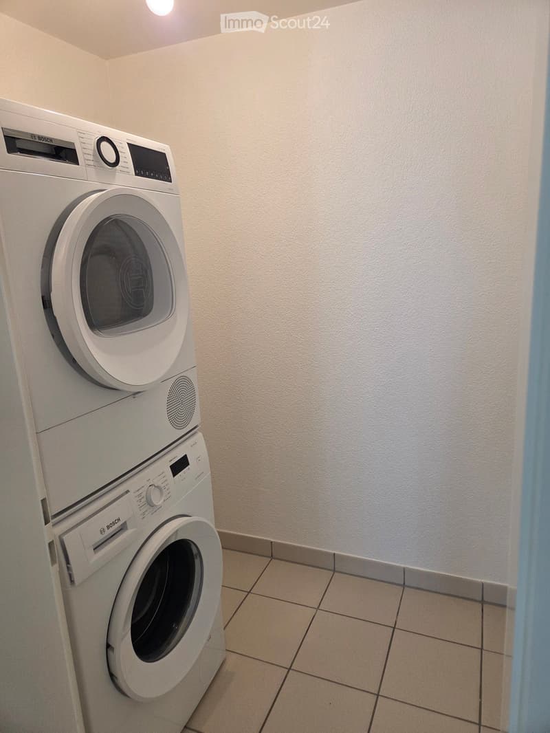 A small bathroom with a stacked washing machine and dryer unit against a white wall.