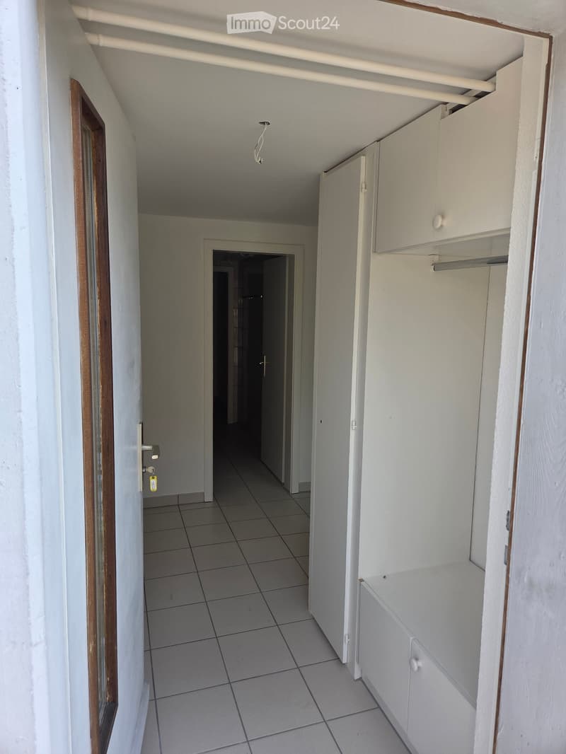 Empty hallway with tiled floor, white walls, and a small built-in cabinet on the right side.