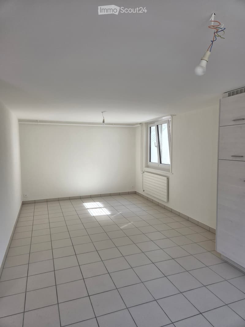 Empty room with tiled floor, white walls, a window with blinds, a radiator, and a light fixture with exposed wiring.