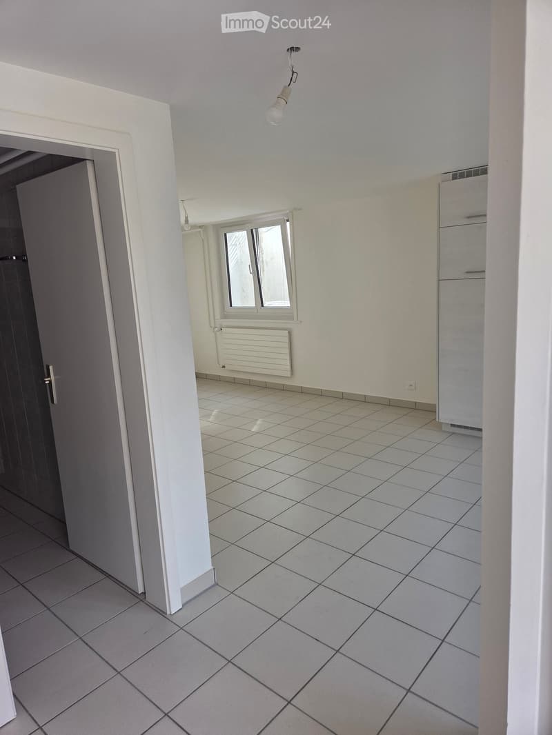 Empty hallway with tiled flooring, white walls, a small window, and a closed door leading to another room.