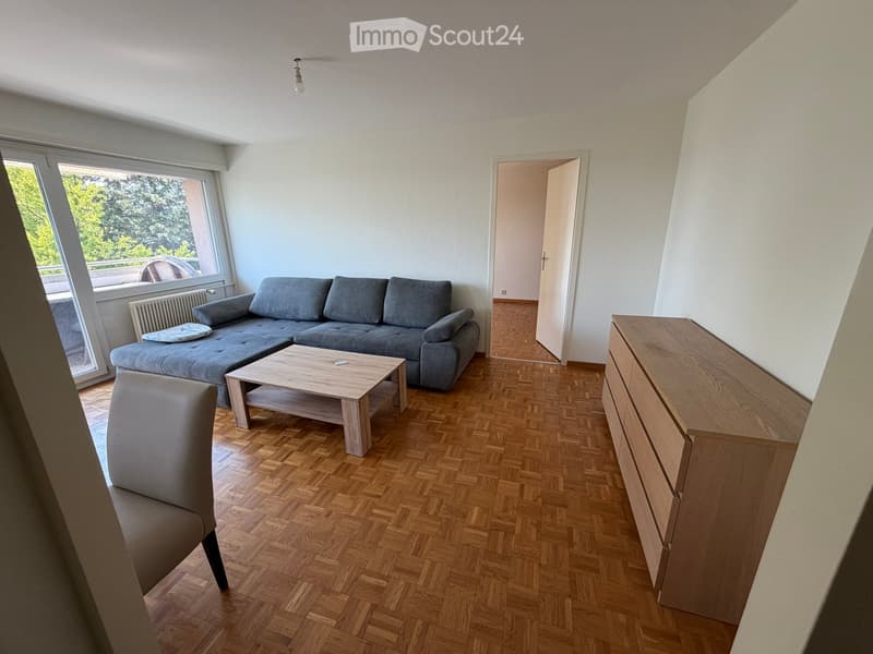 Living room with wooden herringbone flooring, grey sectional sofa, light wooden coffee table, single armchair, and a wooden drawer unit.
