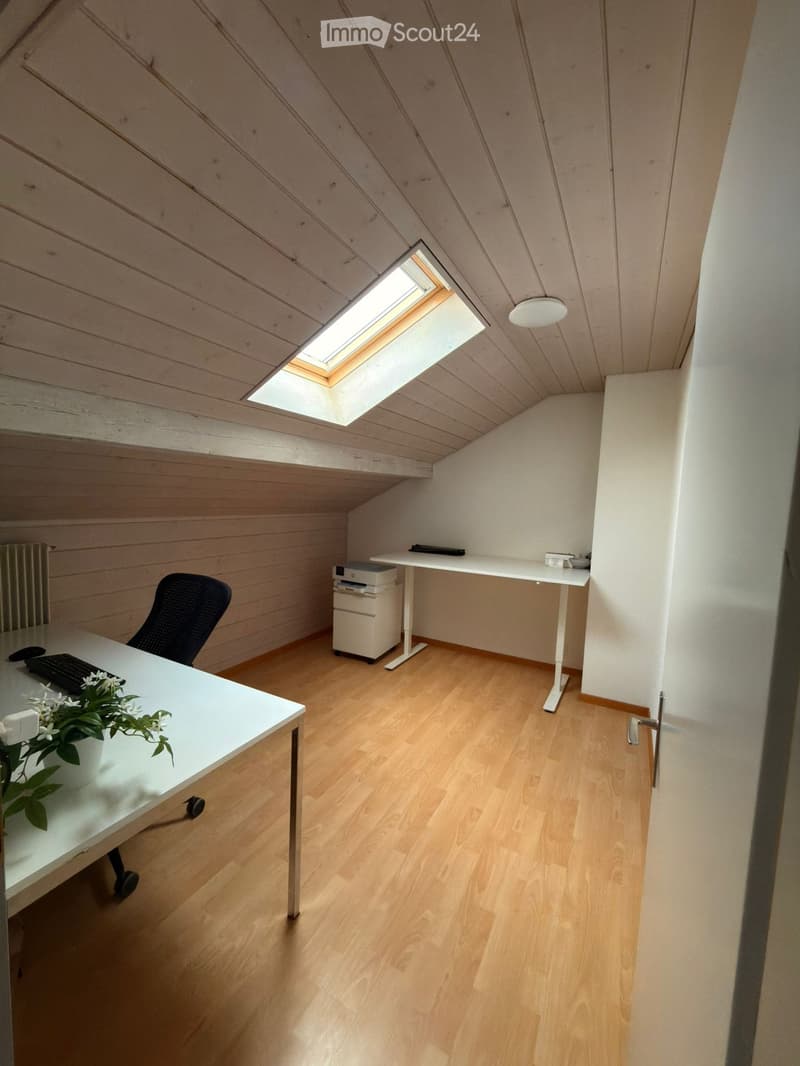 Bright, modern attic room with wooden floors, slanted wooden ceiling, skylight window, and two desks with office equipment.