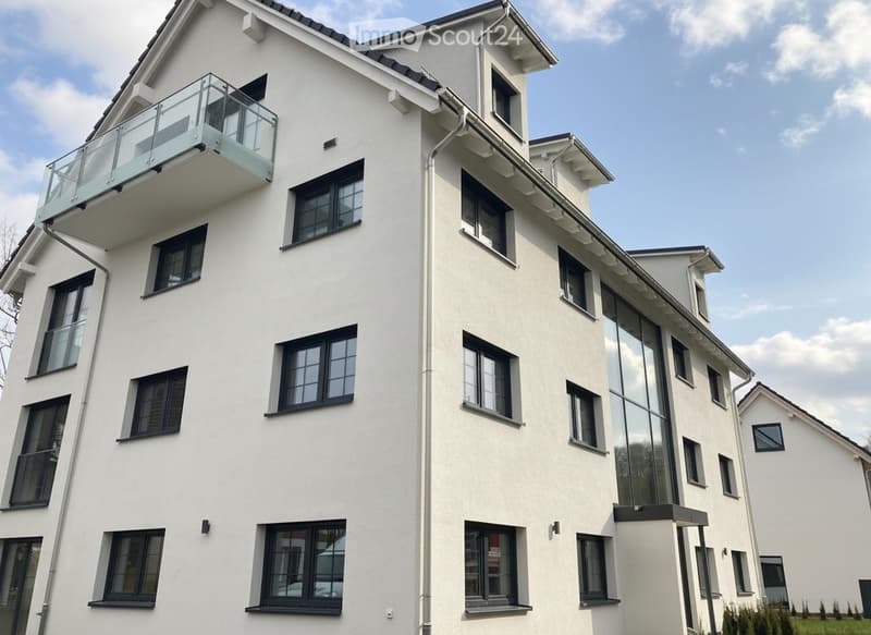 Modern multi-story building with white facade, large windows, and a balcony on the upper floor.