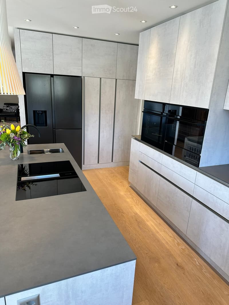 Modern kitchen with grey cabinets, stainless steel appliances, and a central island with a sink and faucet. A vase with flowers is placed on the counter.