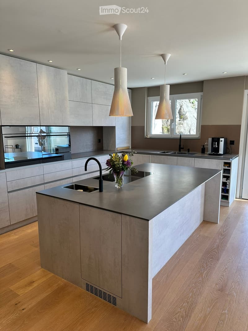 Modern kitchen with grey cabinets, central island, pendant lights, and a vase of flowers on the island.