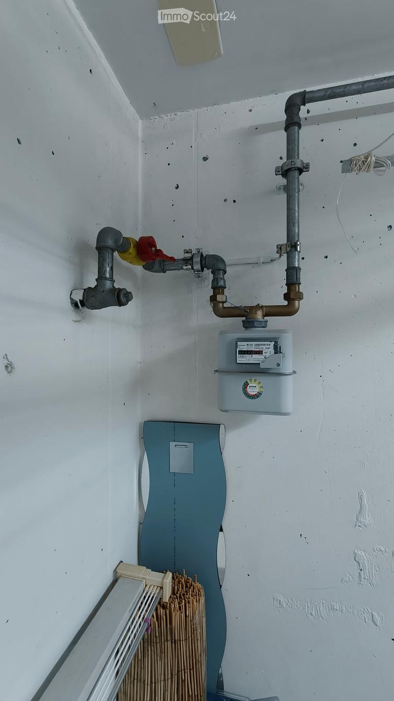 A utility area showing a water heater, water meter, and various pipes mounted on a white wall.