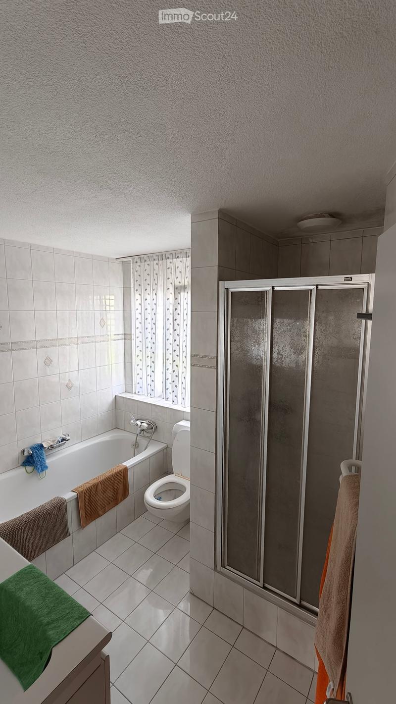 Bathroom with a bathtub, toilet, and a glass-enclosed shower. Towels are placed on the bathtub and near the shower.