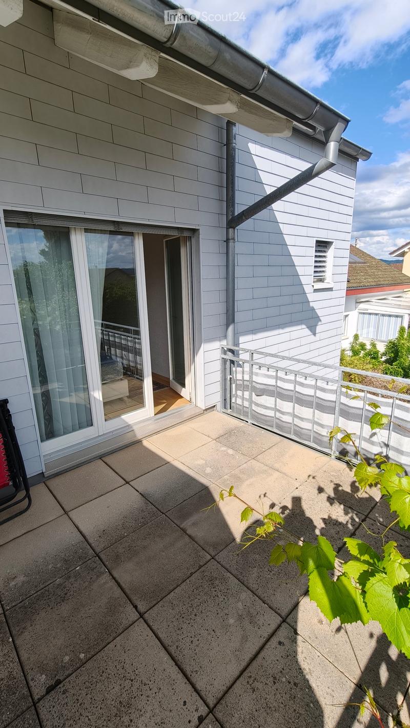 Balcony with tiled floor, metal railing, and a small plant growing on the edge.