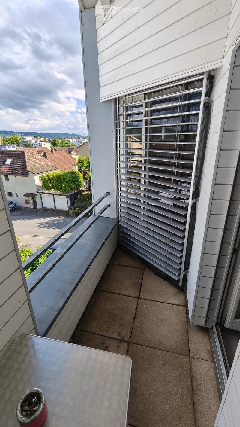 Balcony with tiled floor, metal railing, and a view of the neighborhood. A small table and ashtray are present.