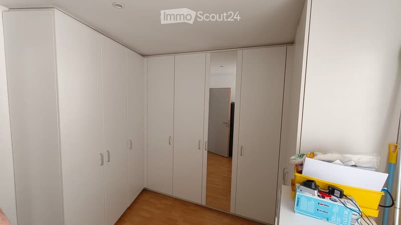 Empty room with white built-in wardrobes, wooden flooring, and a small table with various items on it.