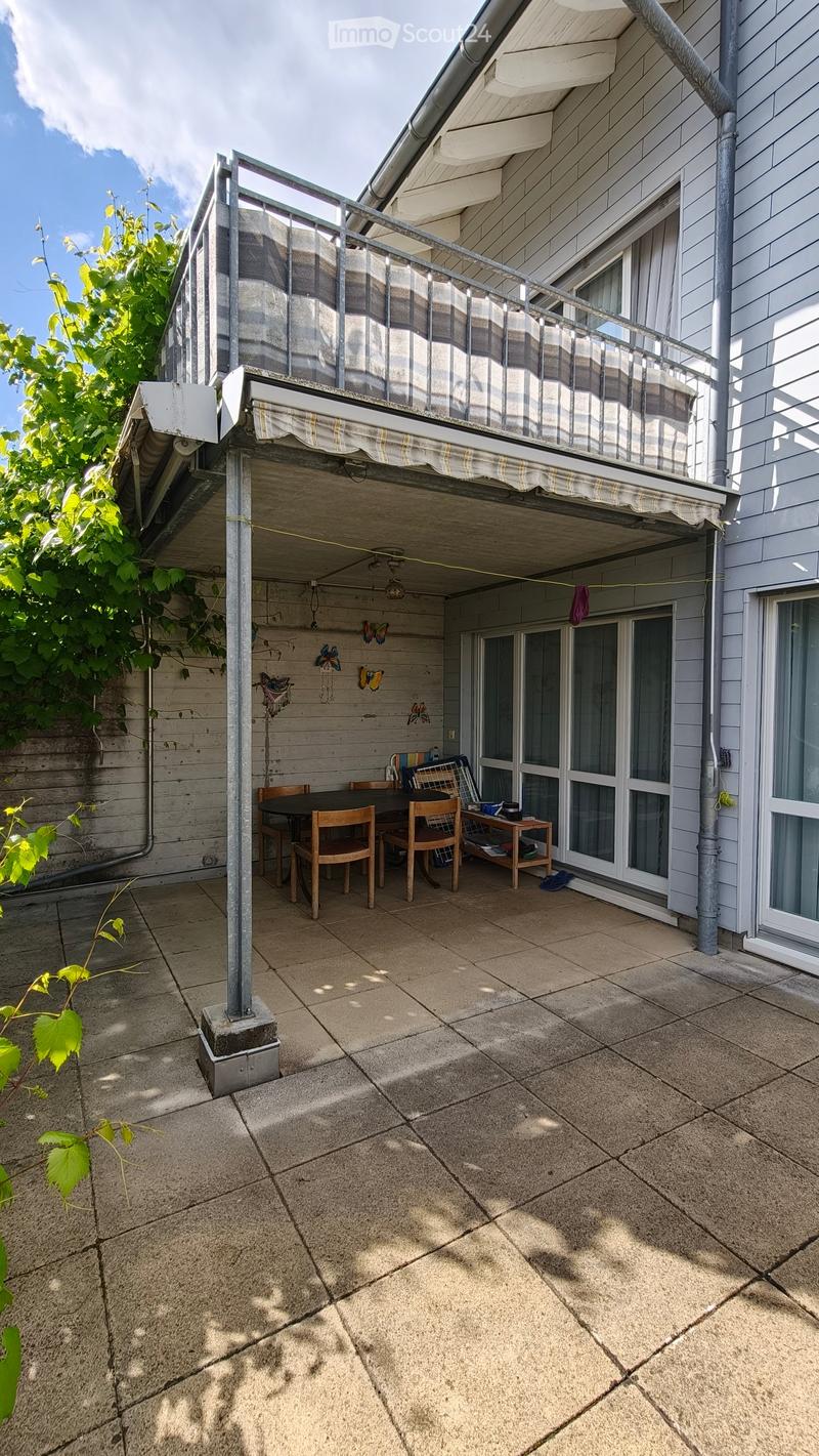 Balcony with a table, chairs, and a small stool, surrounded by a wooden railing and a covered area with a striped awning.