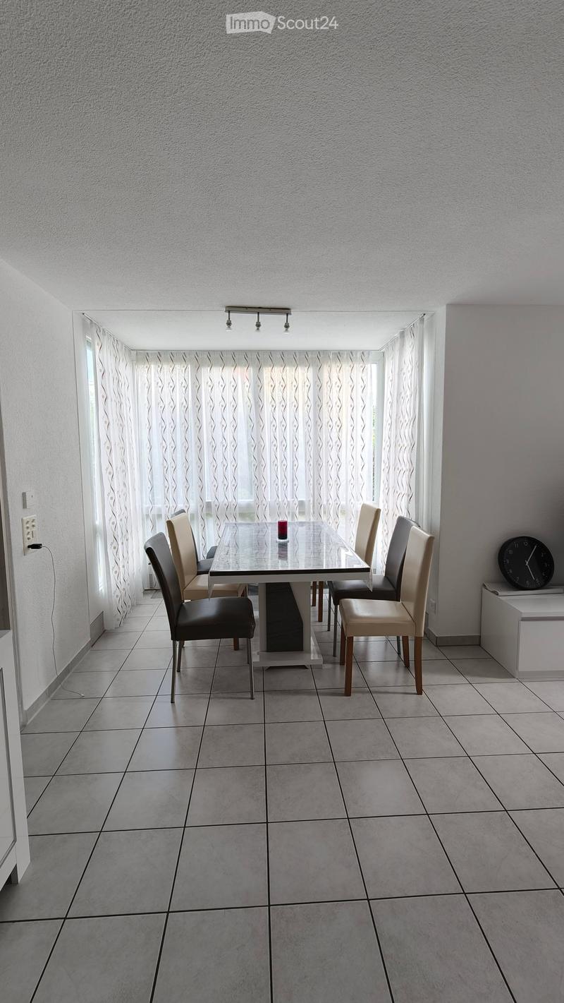 Dining room with a glass dining table, four chairs, and a clock on a white shelf.