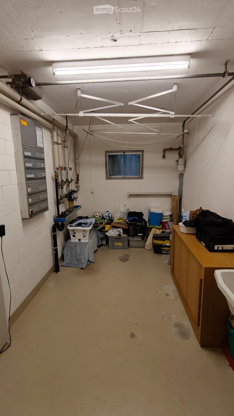 Utility room with exposed pipes, a window, a sink, a cabinet, and various storage items including laundry baskets and bins.