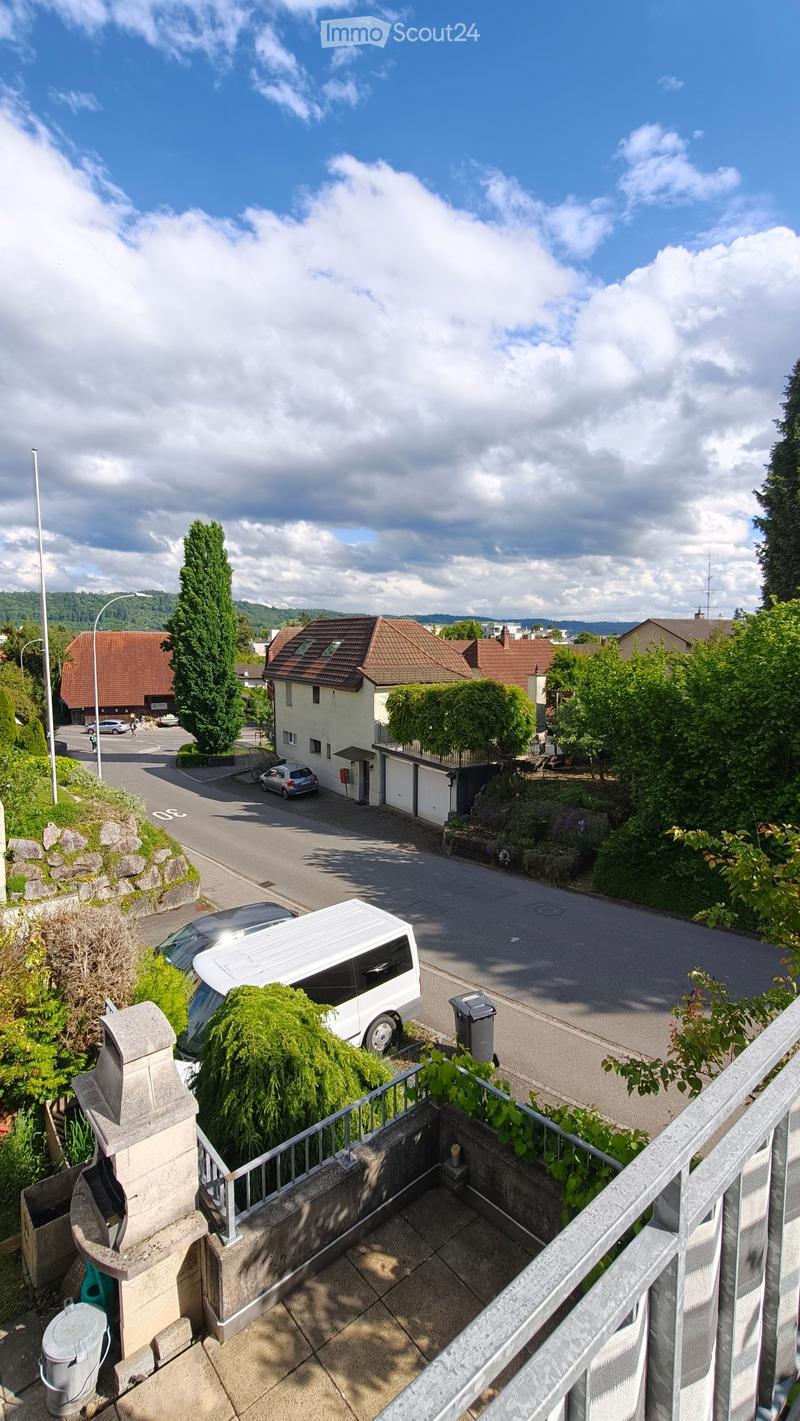 Balcony overlooking a residential street with houses, parked cars, and greenery.
