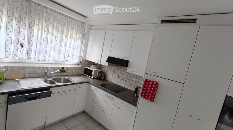 Modern kitchen with white cabinets, stainless steel sink, microwave, dishwasher, and refrigerator. Includes a countertop with a cutting board, oven mitt, and cup.
