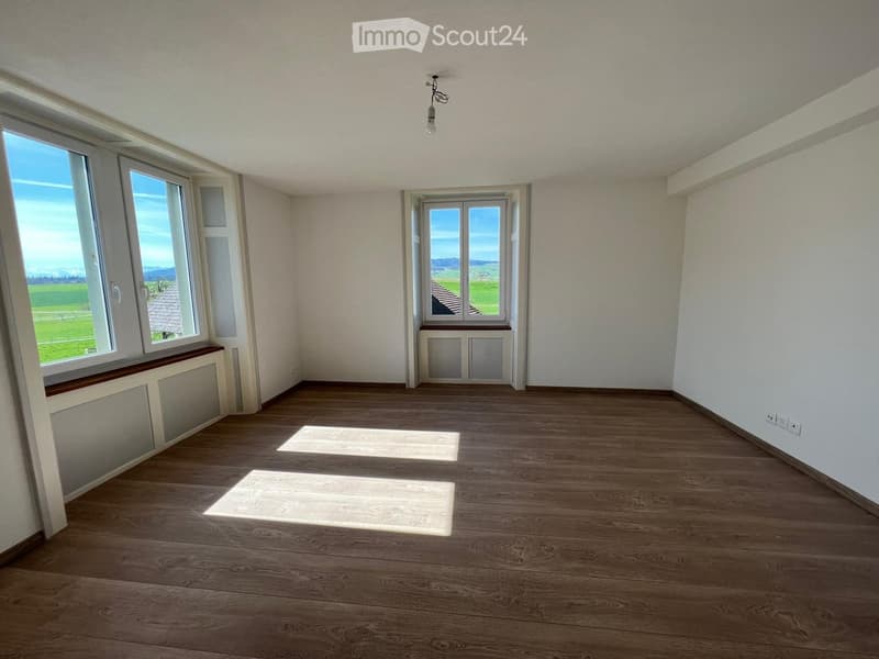 Empty room with wooden flooring, large windows, and radiators. No furniture or equipment present.