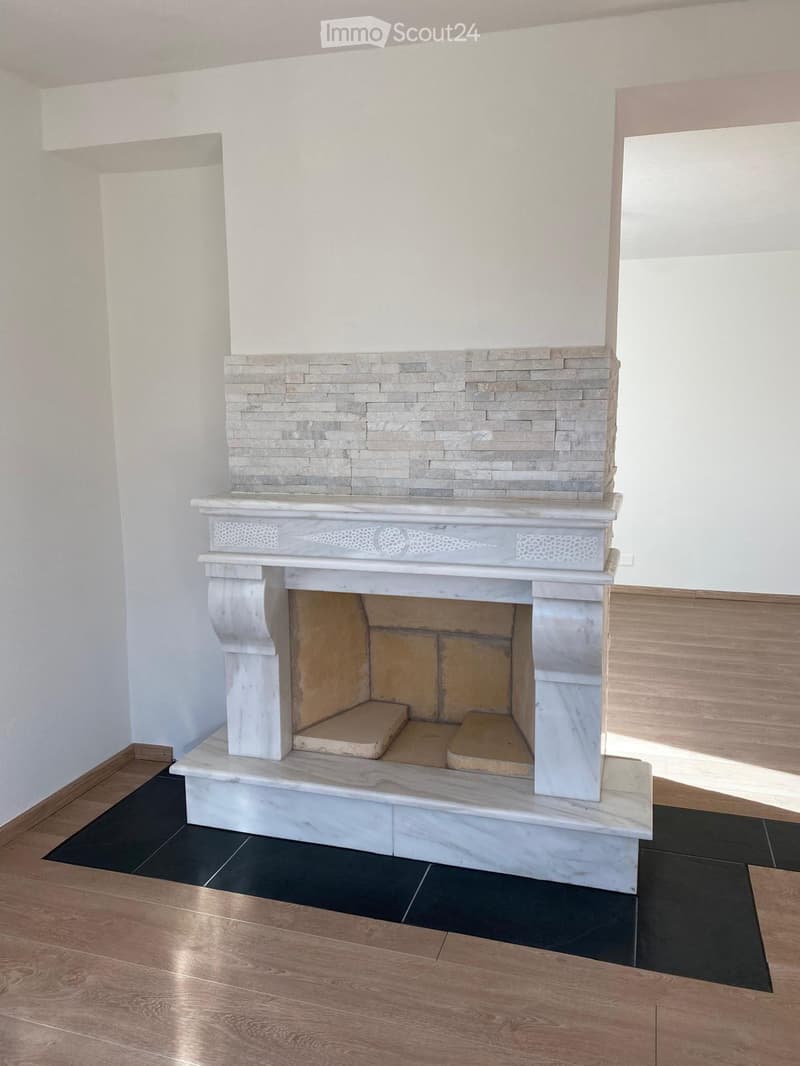 A modern fireplace with a marble surround and decorative stonework, set against white walls and a mix of dark and light flooring.