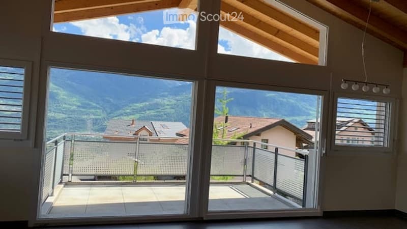 Bright, spacious balcony with large glass doors opening to a scenic mountain view. The balcony features a modern metal railing and tiled flooring.