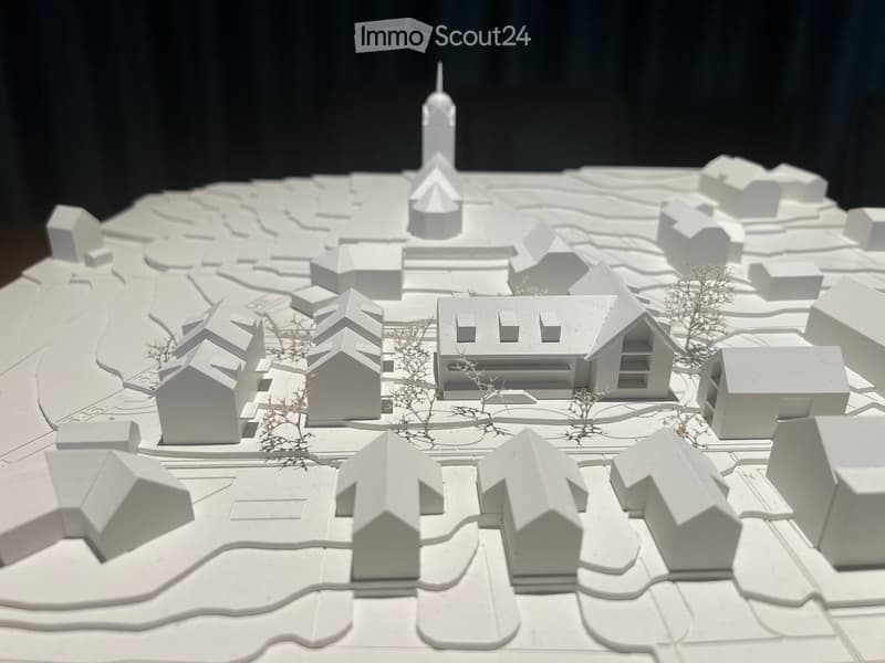Architectural model of a small town with multiple houses, a church tower, and surrounding landscape.