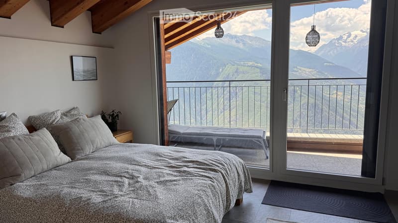 Bright bedroom with a large bed, nightstand, picture frame, and a daybed on the balcony overlooking mountain views.
