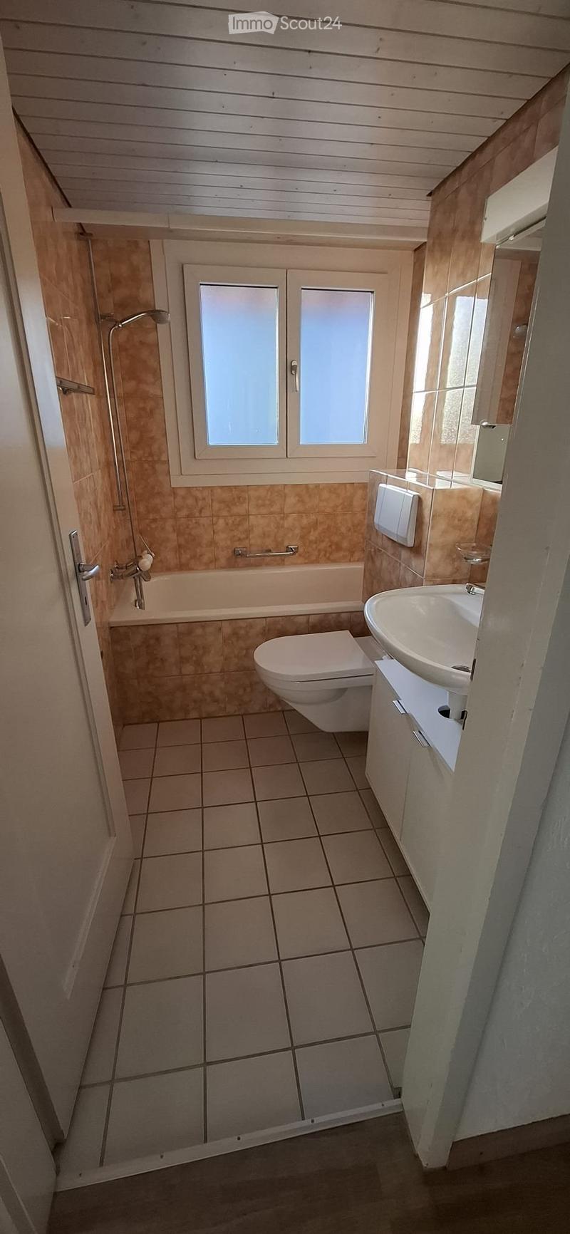 Modern bathroom with beige tiles, a toilet, a sink, a bathtub, and a mirror. Features a window with frosted glass and a showerhead.