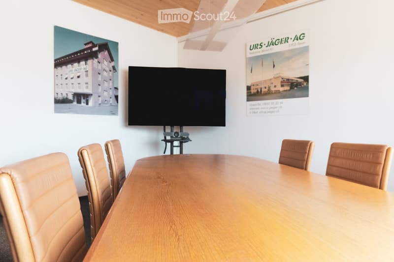 Conference room with a large wooden table, leather chairs, a mounted screen, and speaker system.