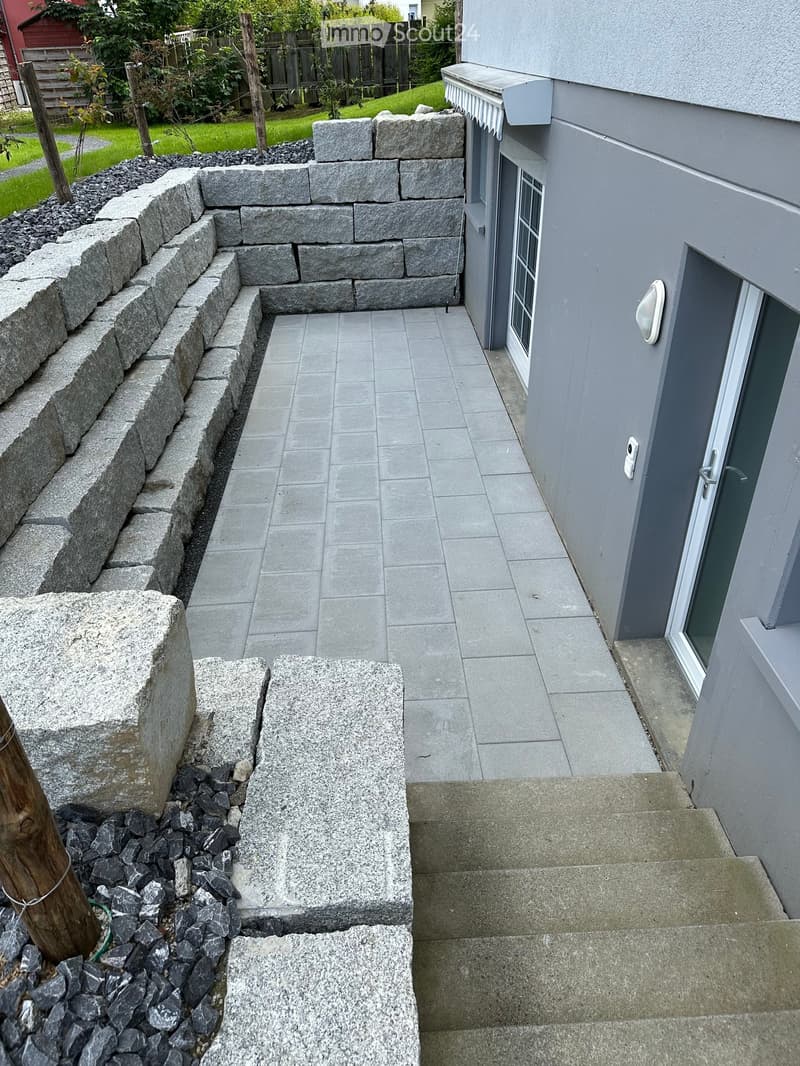 Stone steps leading up to a house entrance, with a stone retaining wall and gravel border.