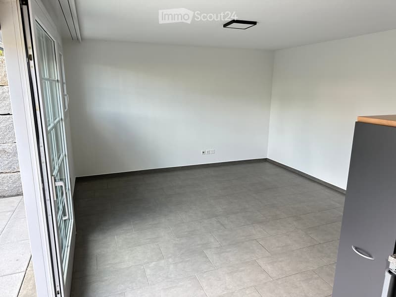 Empty room with grey tiled floor, white walls, large window, and modern ceiling light fixture.