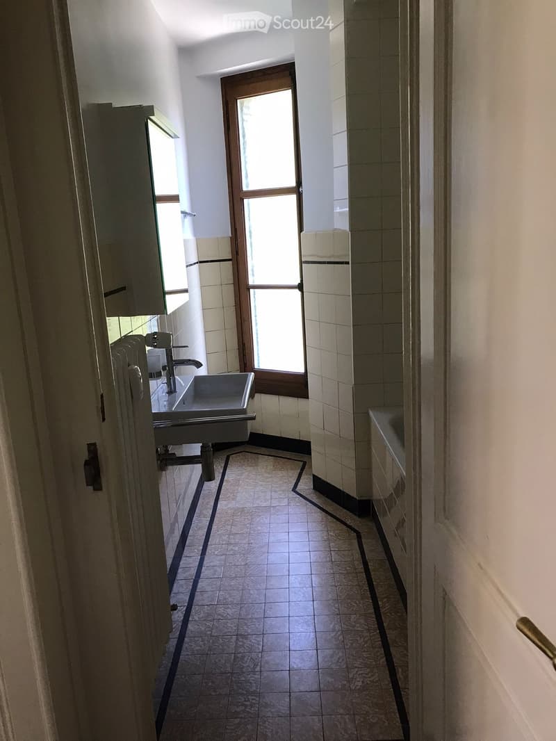 Bathroom with a sink, faucet, and tiled walls and floor. The space is well-lit with natural light coming through a frosted glass door.