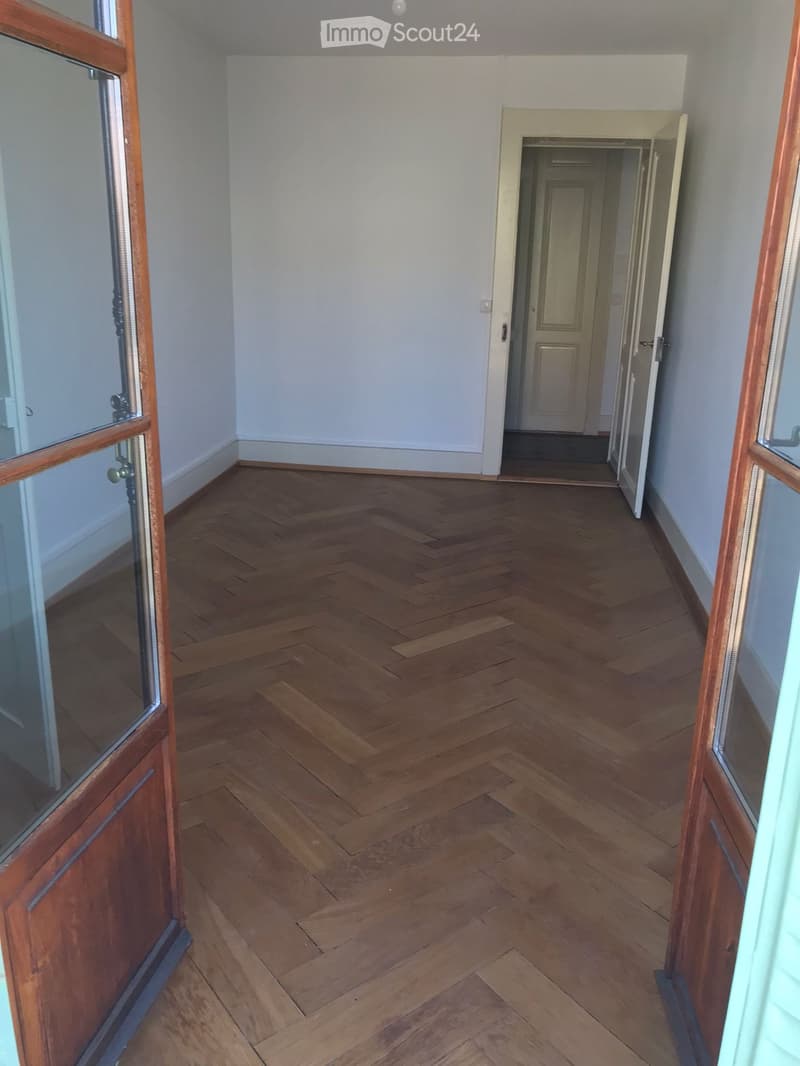 Empty hallway with wooden herringbone flooring, white walls, and open doors leading to other rooms.